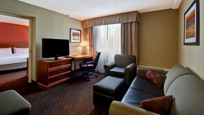 A hotel room with a bed, a desk with a TV, a chair, a sofa, and a window with curtains. - Holiday Inn Cincinnati-Riverfront by IHG (Covington)