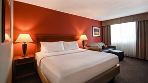A hotel room with a large bed, two bedside tables with lamps, a sofa, and a window with curtains. - Holiday Inn Cincinnati-Riverfront by IHG (Covington)
