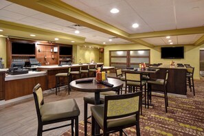 A hotel lobby with a bar area, seating arrangements, and a television screen.