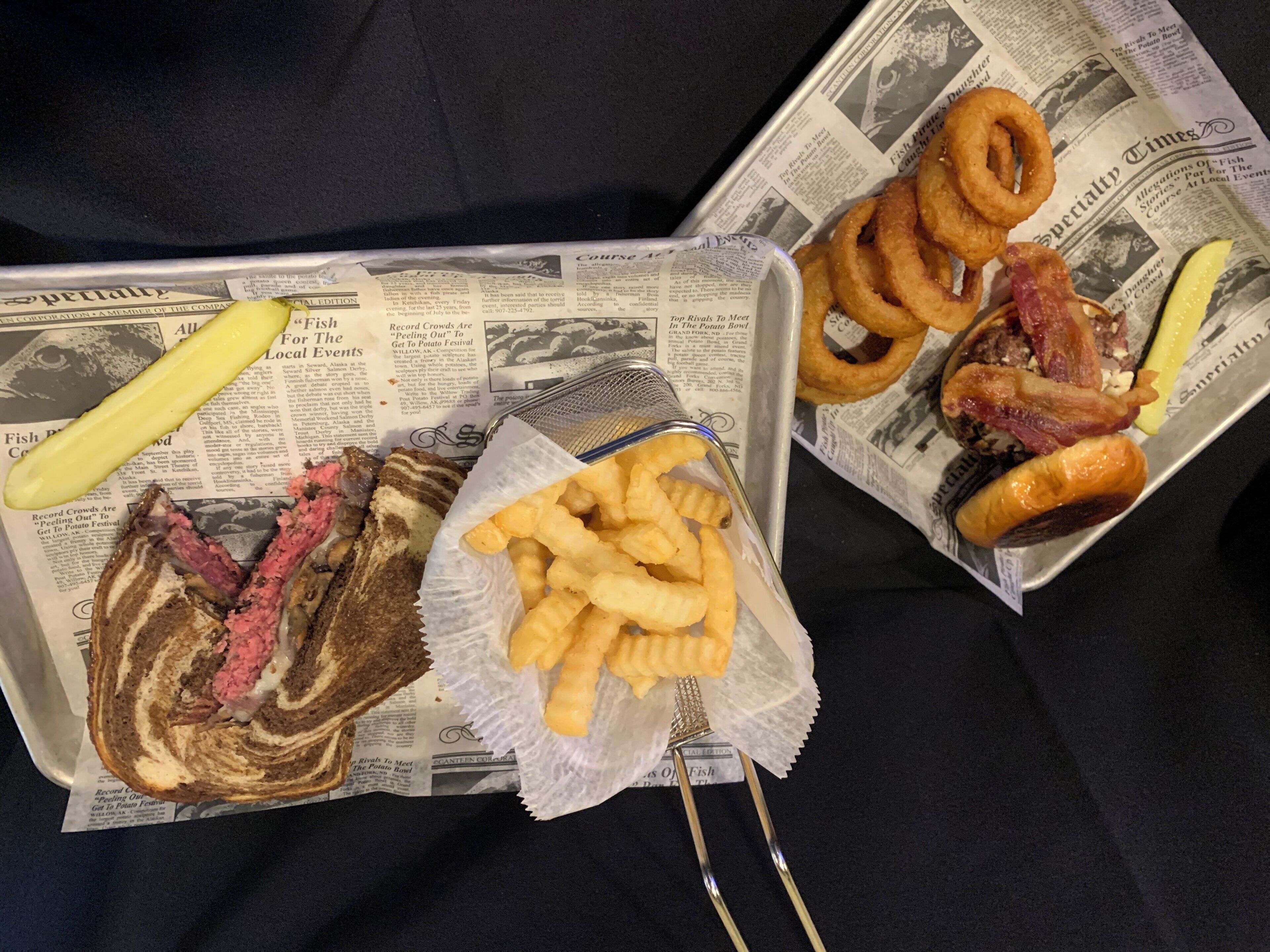 A tray with a sandwich, fries, onion rings, and a pickle on a newspaper.