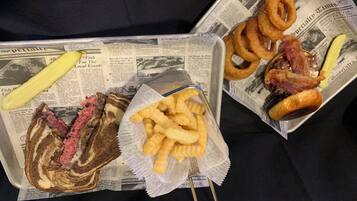 A tray with a sandwich, fries, onion rings, and a pickle on a newspaper.
