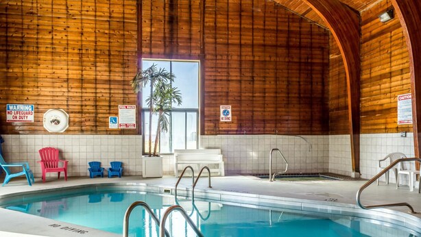 Una piscina interior con paredes de madera, un cartel indicando la presencia de socorrista, normas de la piscina y sillas alrededor.