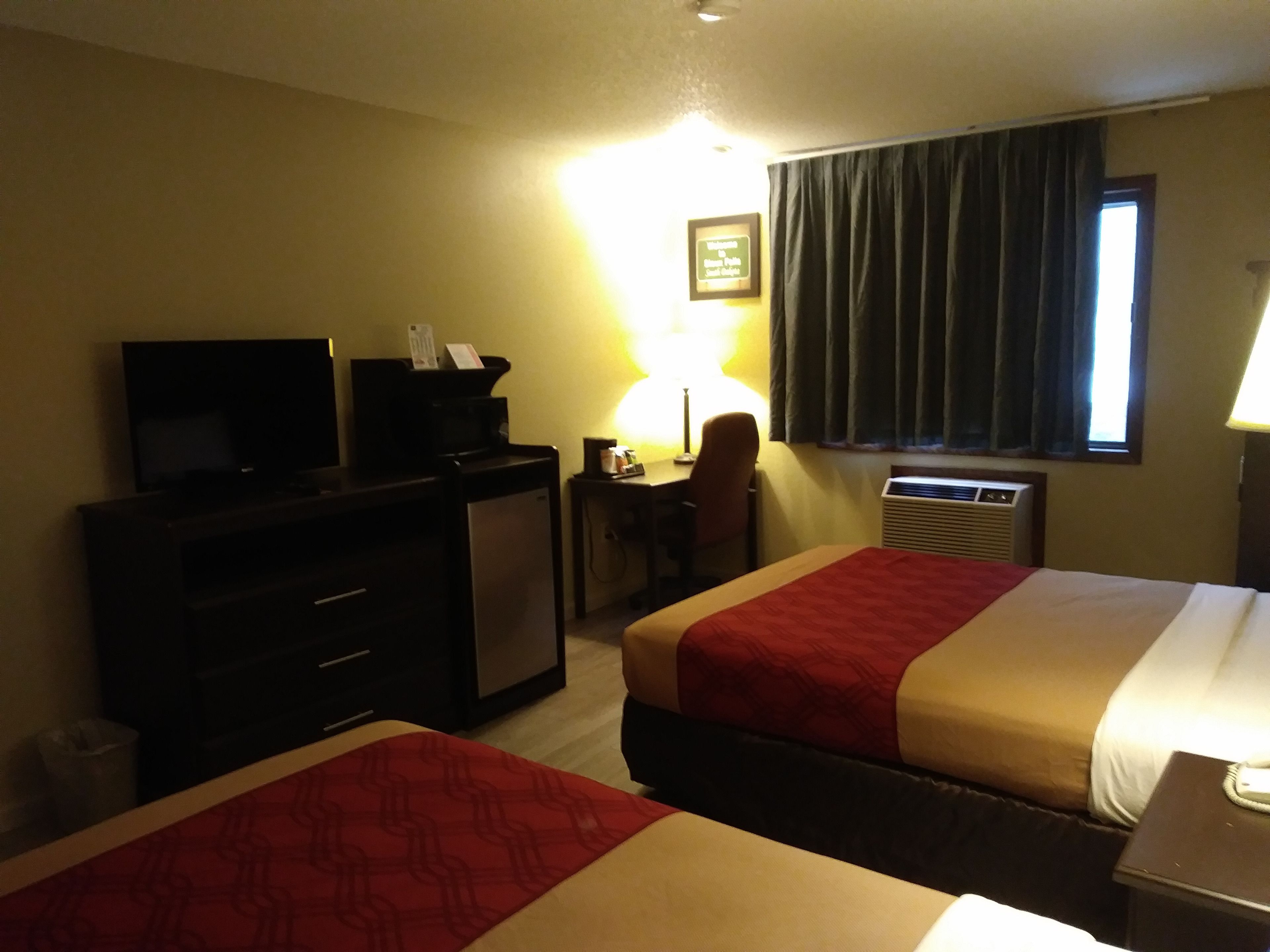 A hotel room with two beds, a desk, a television, a lamp, and an air conditioning unit.