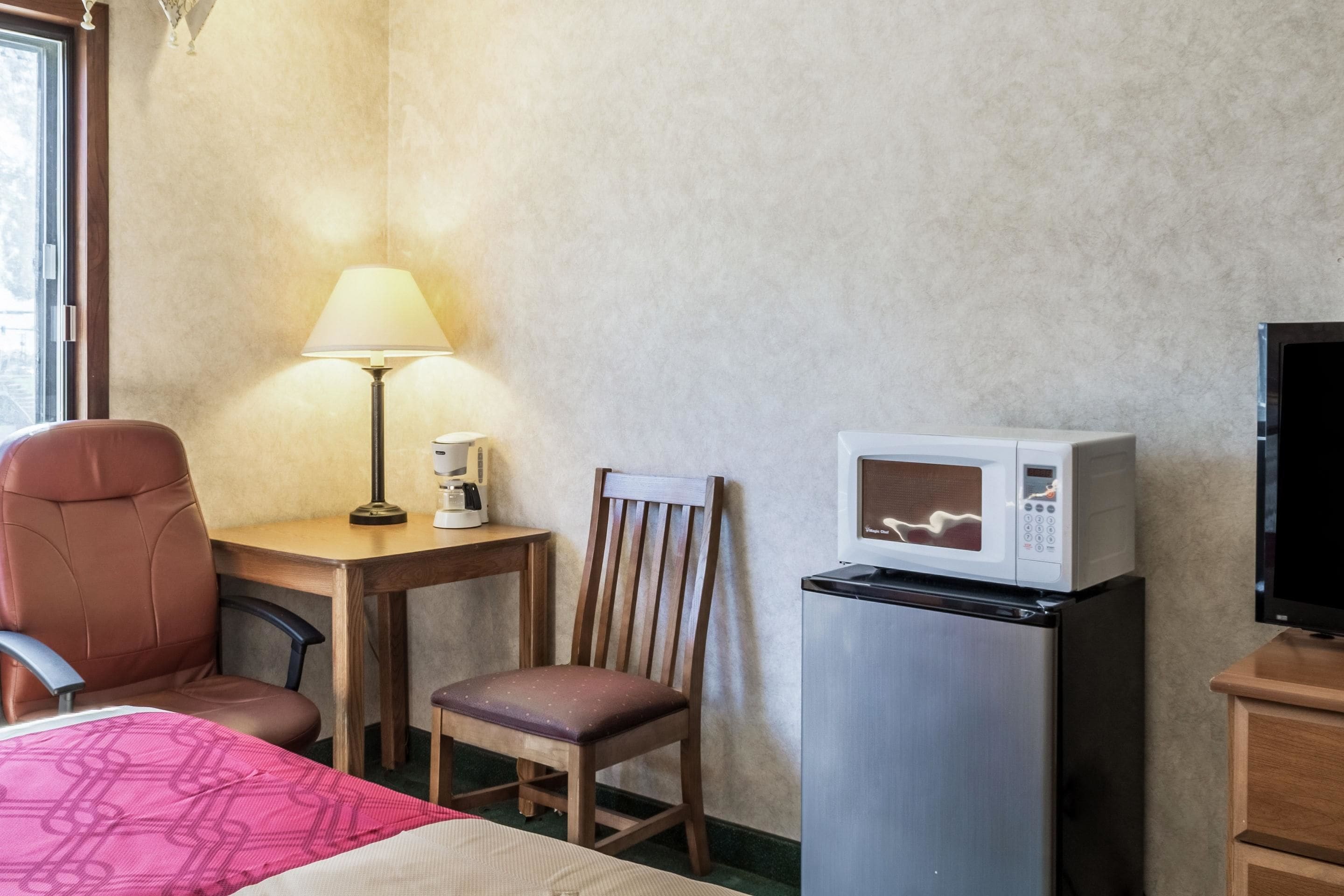 Een hotelkamer met een bed, een bureau met lamp, een stoel, een magnetron, een koelkast en een televisie.