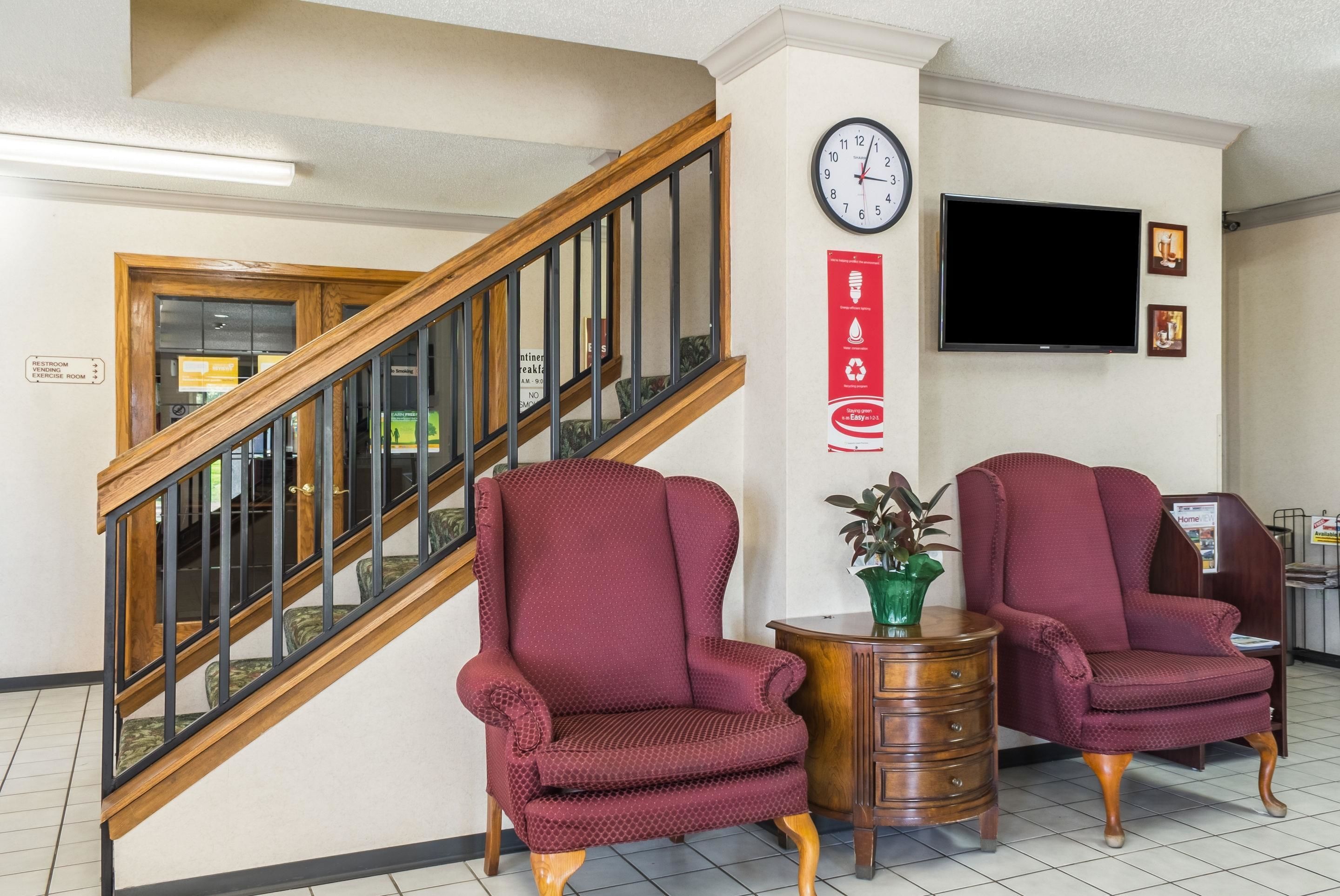 Un vestíbulo con una escalera, dos sillones, un reloj y un televisor de pantalla plana montado en la pared.