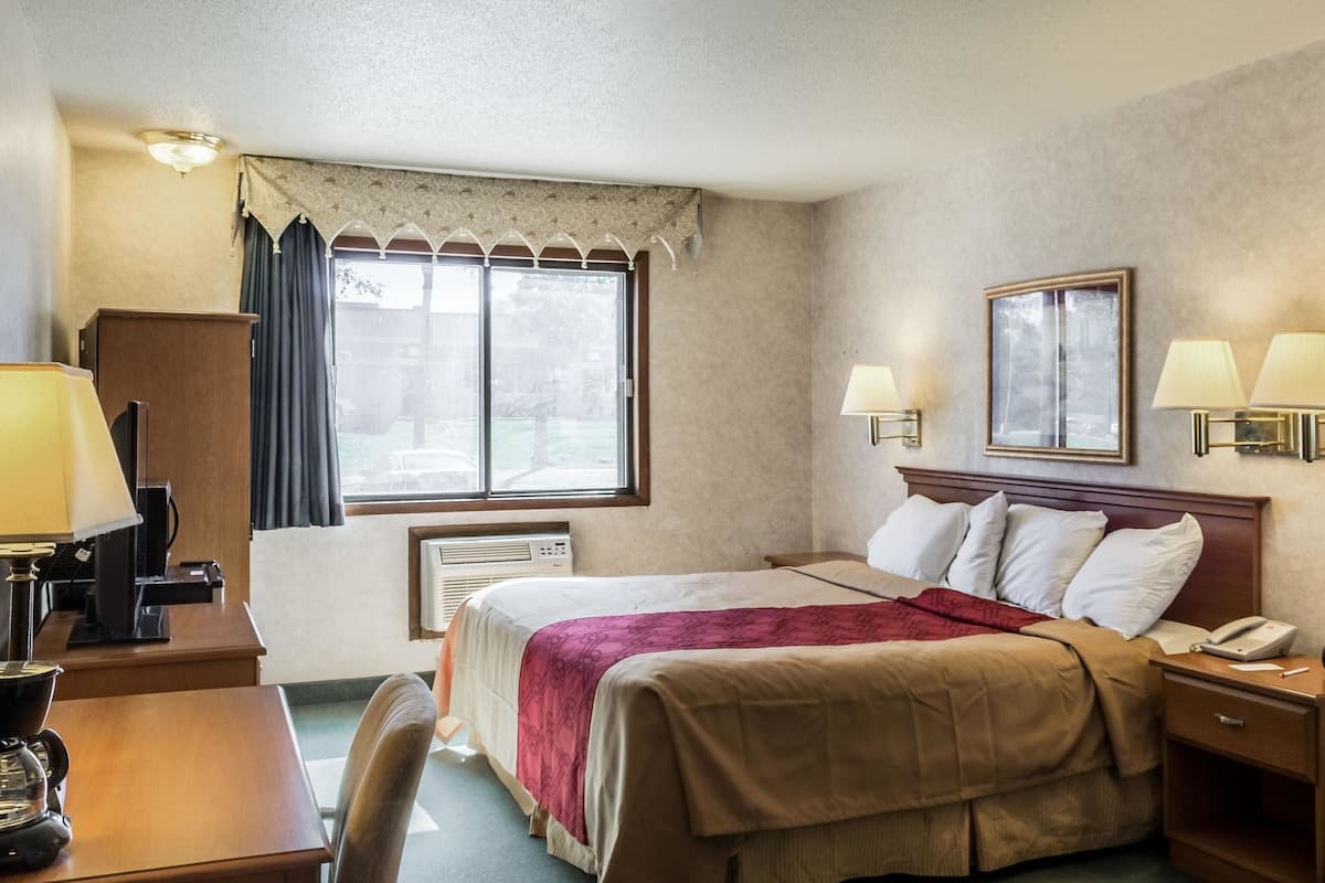 A hotel room with a bed, bedside lamps, a desk with a lamp, a telephone, and a window with curtains.