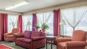 Una habitación de hotel con un sofá rojo, dos sillones, una mesita pequeña y una alfombra roja con un mensaje de bienvenida.