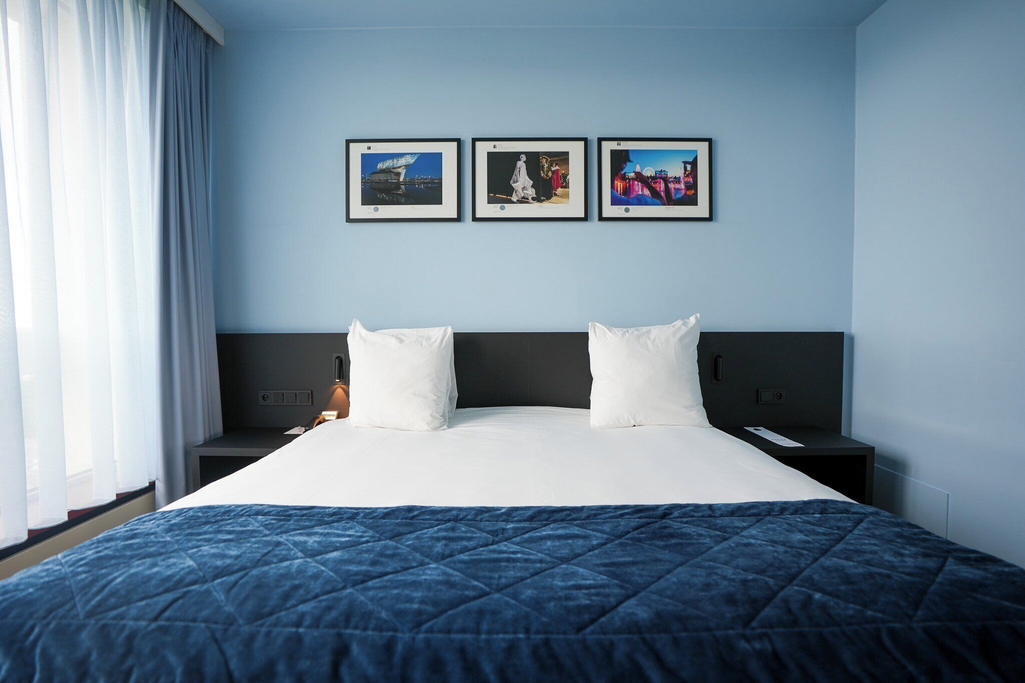 A hotel room with a large bed, a nightstand, a bedside table, and three framed pictures on the wall.