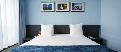A hotel room with a large bed, a nightstand, a bedside table, and three framed pictures on the wall.