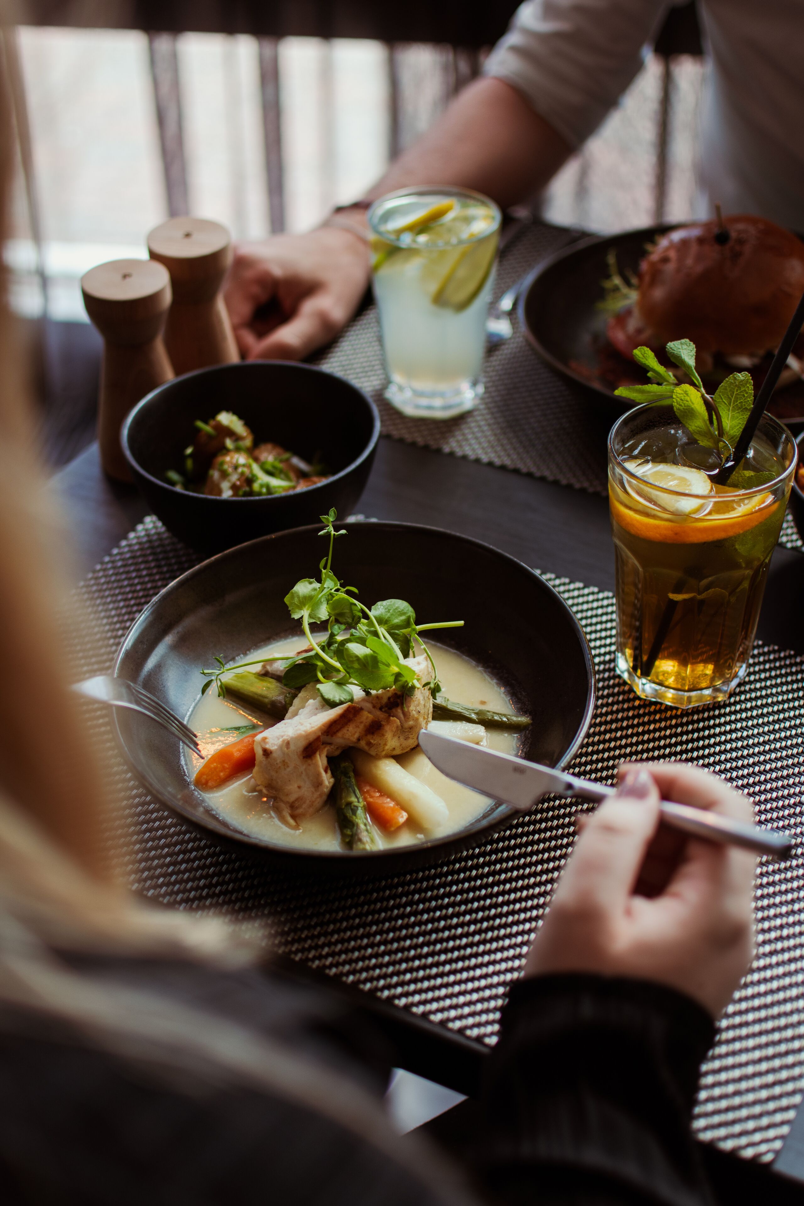 A dining table with a bowl of soup, a glass of iced tea, and a plate with a burger.