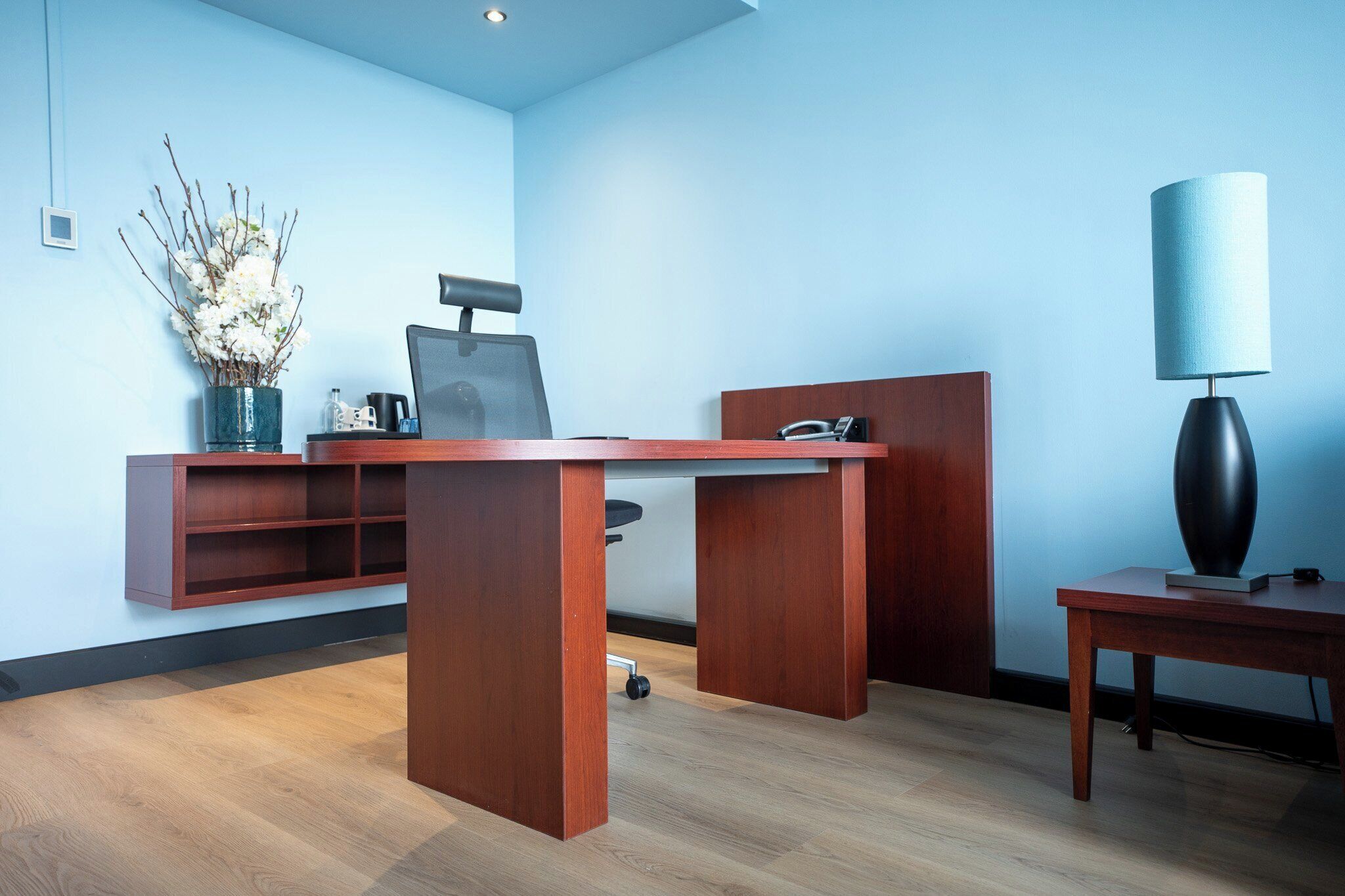 A modern office space with a wooden desk, a chair, a lamp, and a decorative vase.