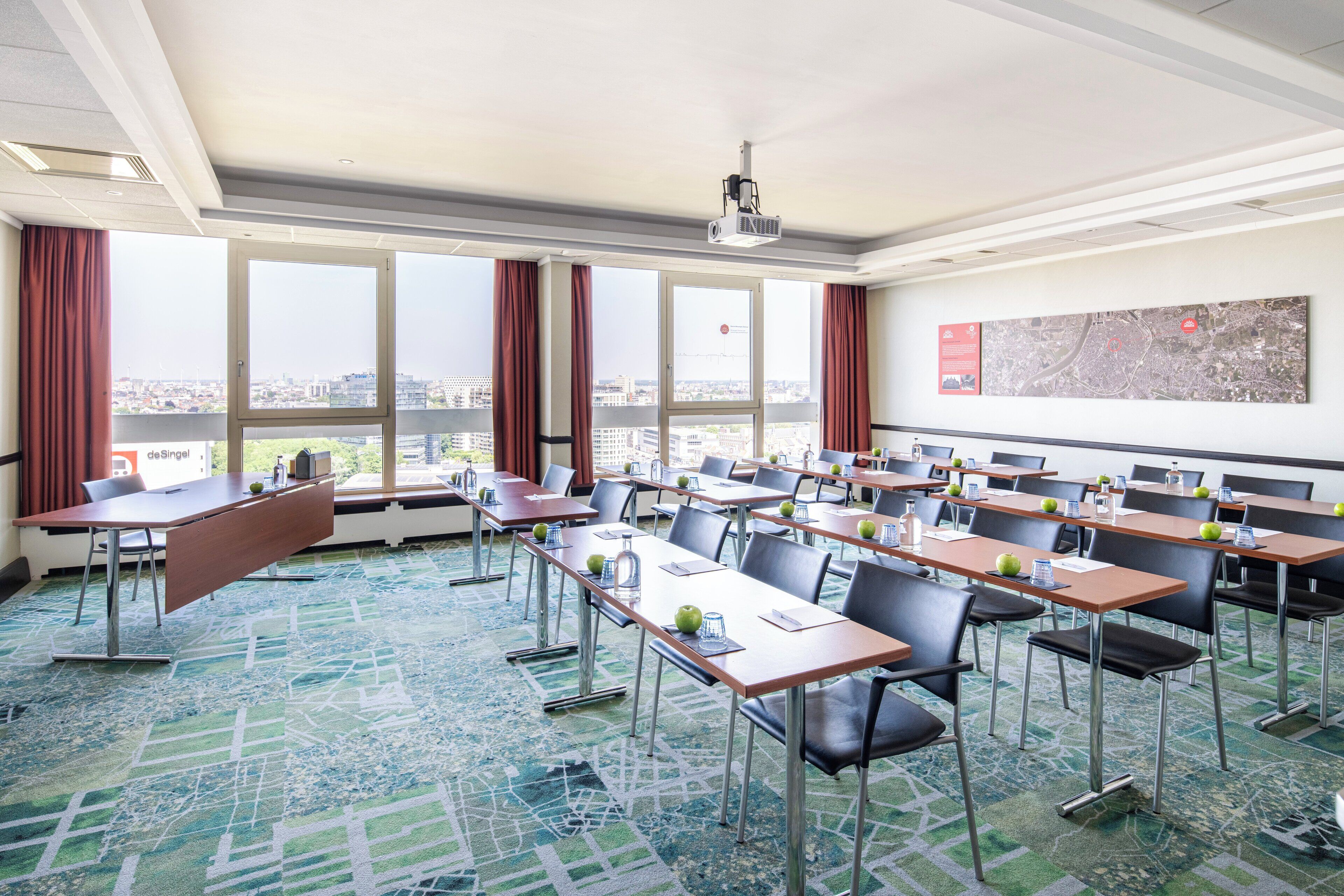 A conference room with tables, chairs, a projector, and large windows with curtains.