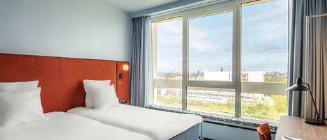 Et hotelværelse med en stor seng, et skrivebord og et vindue med udsigt over byen.