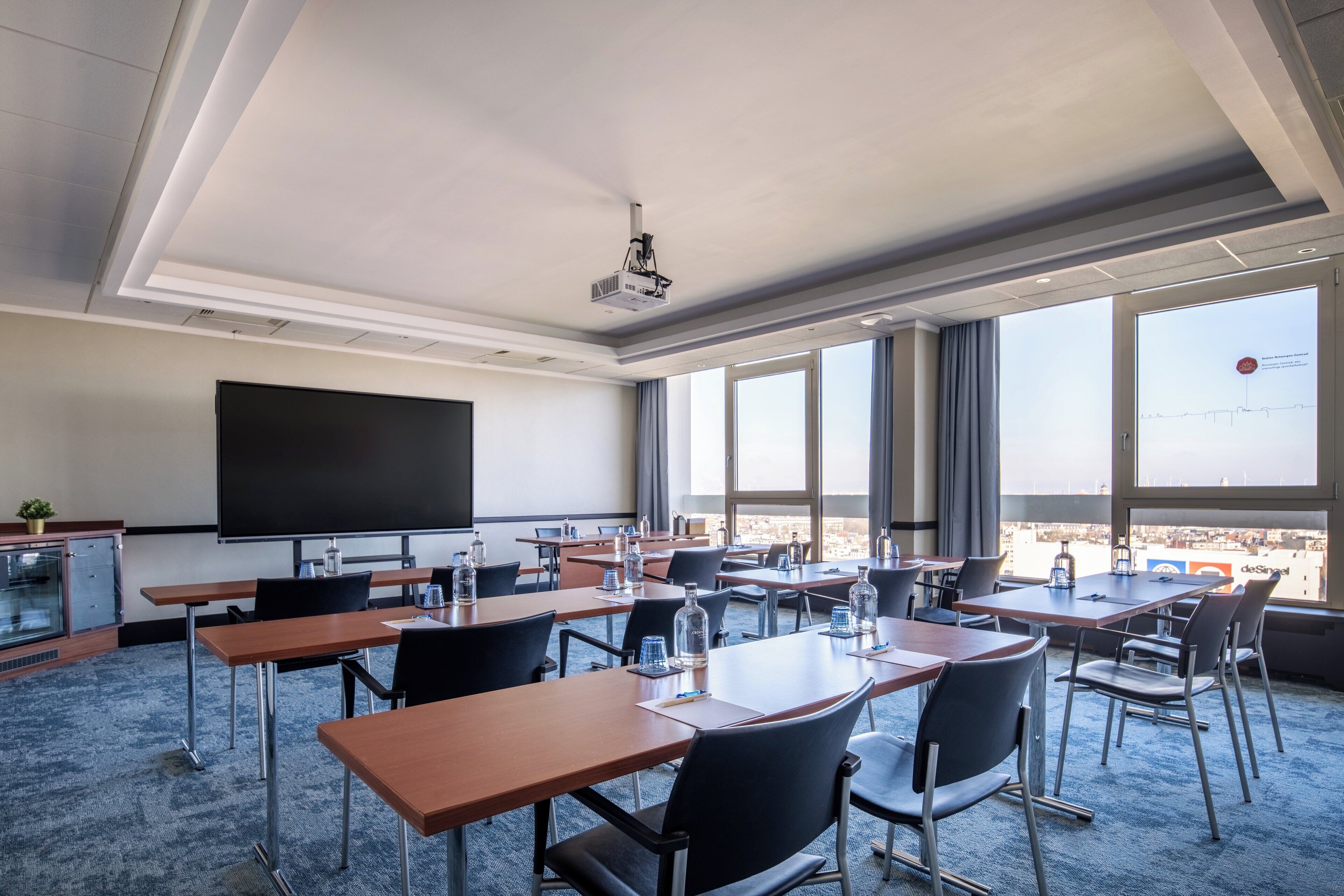 A conference room with a large screen, multiple tables, and chairs.