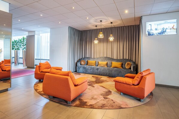 Een moderne lobby met een grijze bank, oranje fauteuils en een kamerbreed tapijt met dessin.