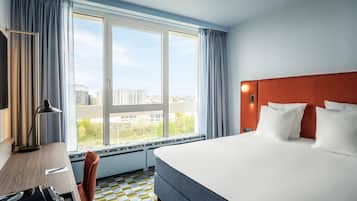 A hotel room with a large bed, a desk, a chair, and a window with curtains.