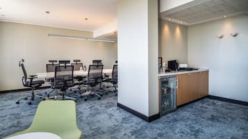 Una sala de conferencias moderna con una mesa larga, varias sillas, una kitchenette y una llamativa silla verde.