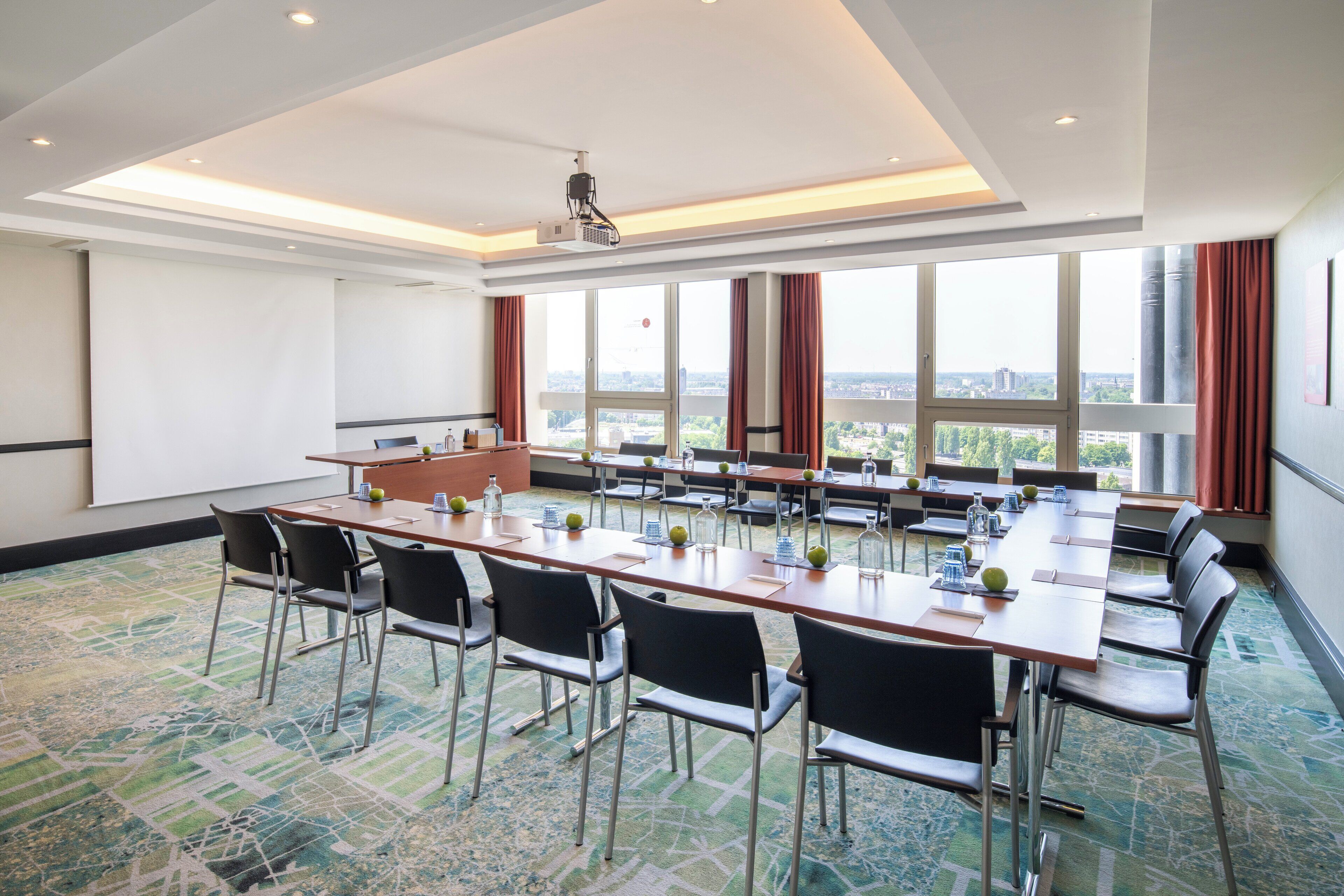 A conference room with a long table, chairs, a projector, and large windows with a city view.