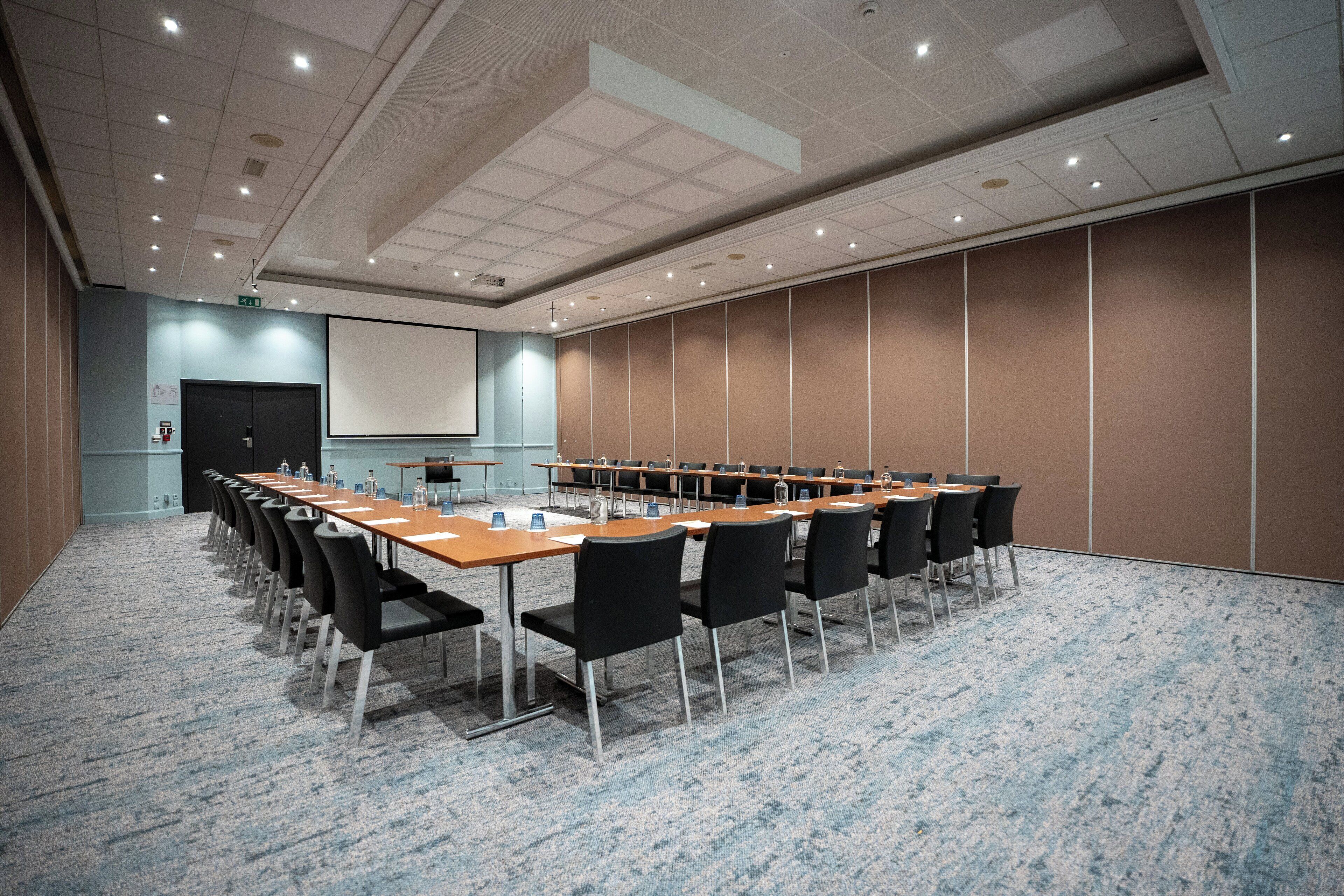 A conference room with a long table, black chairs, and a projector screen.