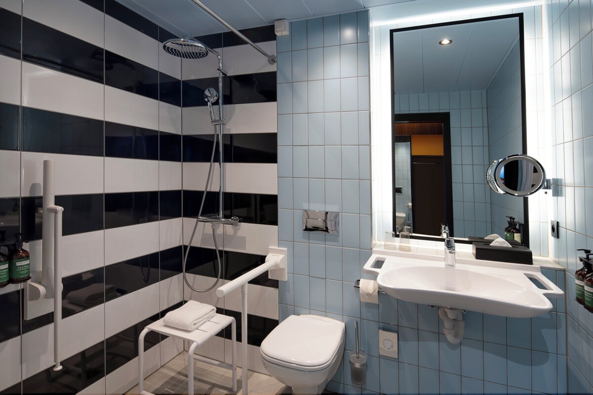 A modern bathroom with a black and white tiled wall, a white sink, and a handheld showerhead.