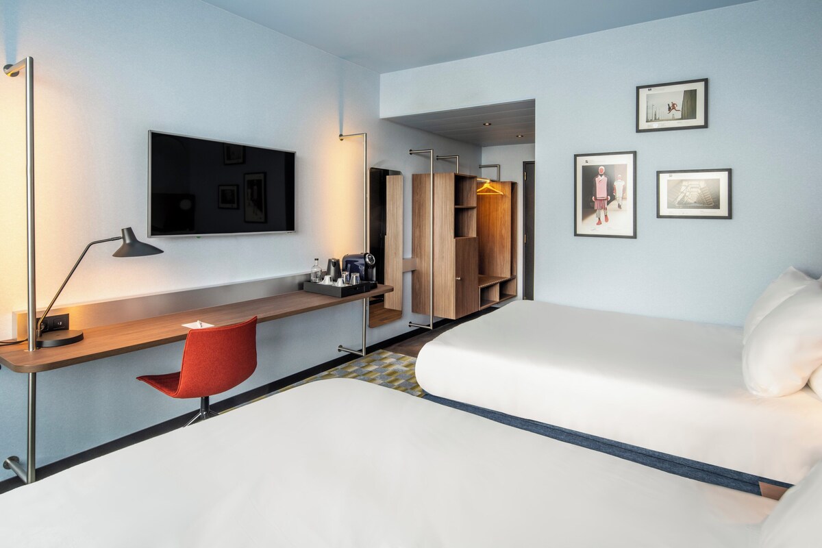 A modern hotel room with a bed, a desk, a chair, a wardrobe, and a TV.