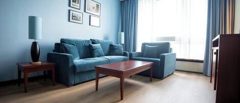 A modern living room with a blue sofa, a wooden coffee table, and a lamp on a side table.
