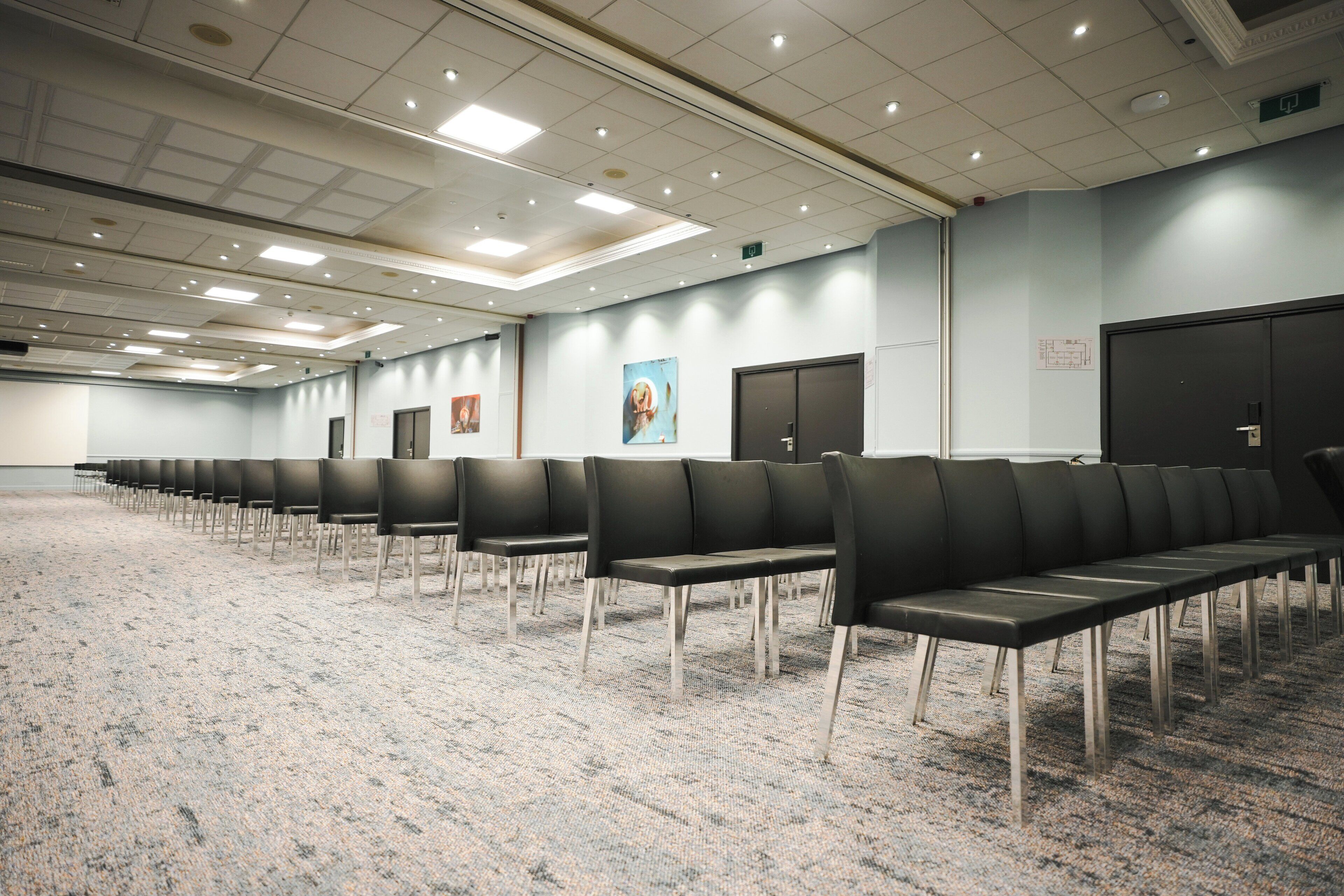 Ein Konferenzraum mit Reihen schwarzer Stühle, Teppichboden und Deckenleuchten.