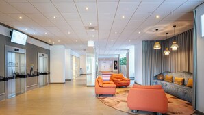 A modern lobby with a reception desk, elevators, orange seating, and a grey sofa with yellow cushions. - Crowne Plaza Antwerp by IHG (Antwerp)