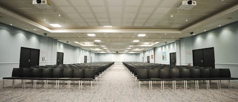 Un salón de conferencias amplio con filas de sillas negras, piso alfombrado y un techo alto con iluminación empotrada.