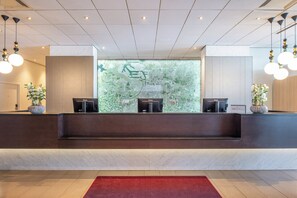 Een receptie met een marmeren balie, twee receptionisten en een groot raam met uitzicht op groen.