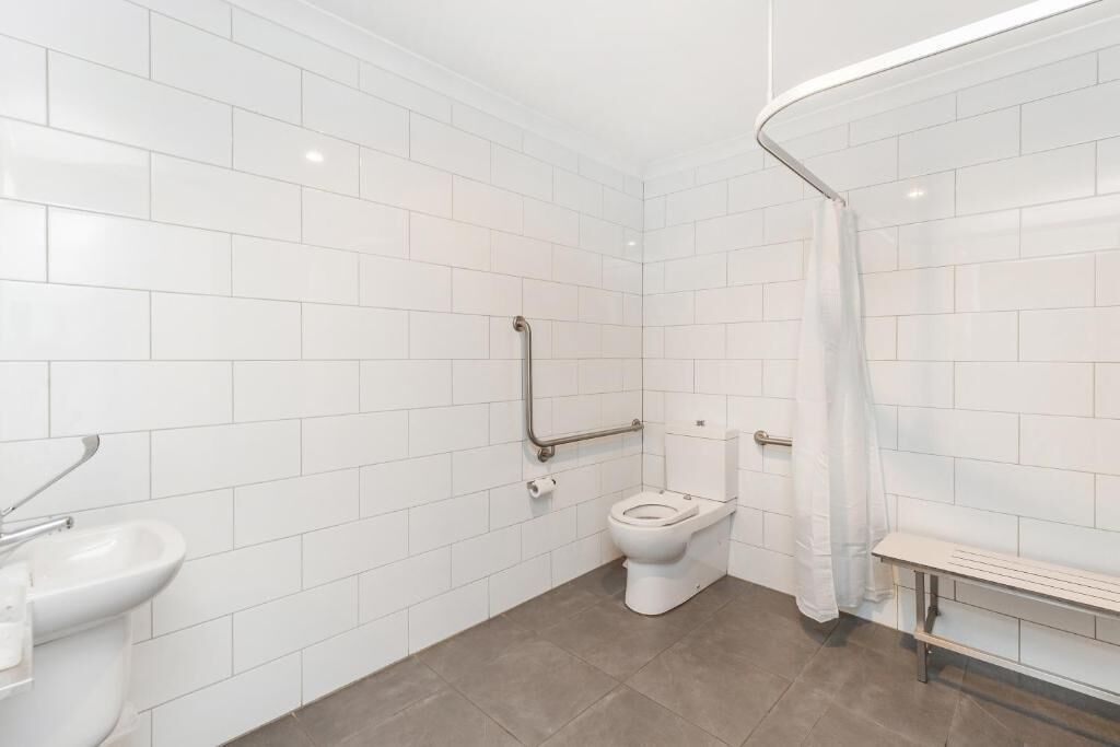 Une salle de bain moderne avec des carreaux blancs, des toilettes, un lavabo et un banc.