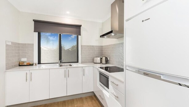 A modern kitchen with white cabinets, a built-in oven, and a stainless steel range hood. - Allara Motor Lodge (White Hills)