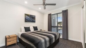 A hotel room with a large bed, a ceiling fan, a window with curtains, and a painting on the wall. - Allara Motor Lodge (White Hills)
