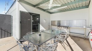 An outdoor patio with a glass table and chairs, a stainless steel grill, and a ceiling fan. - Allara Motor Lodge (White Hills)