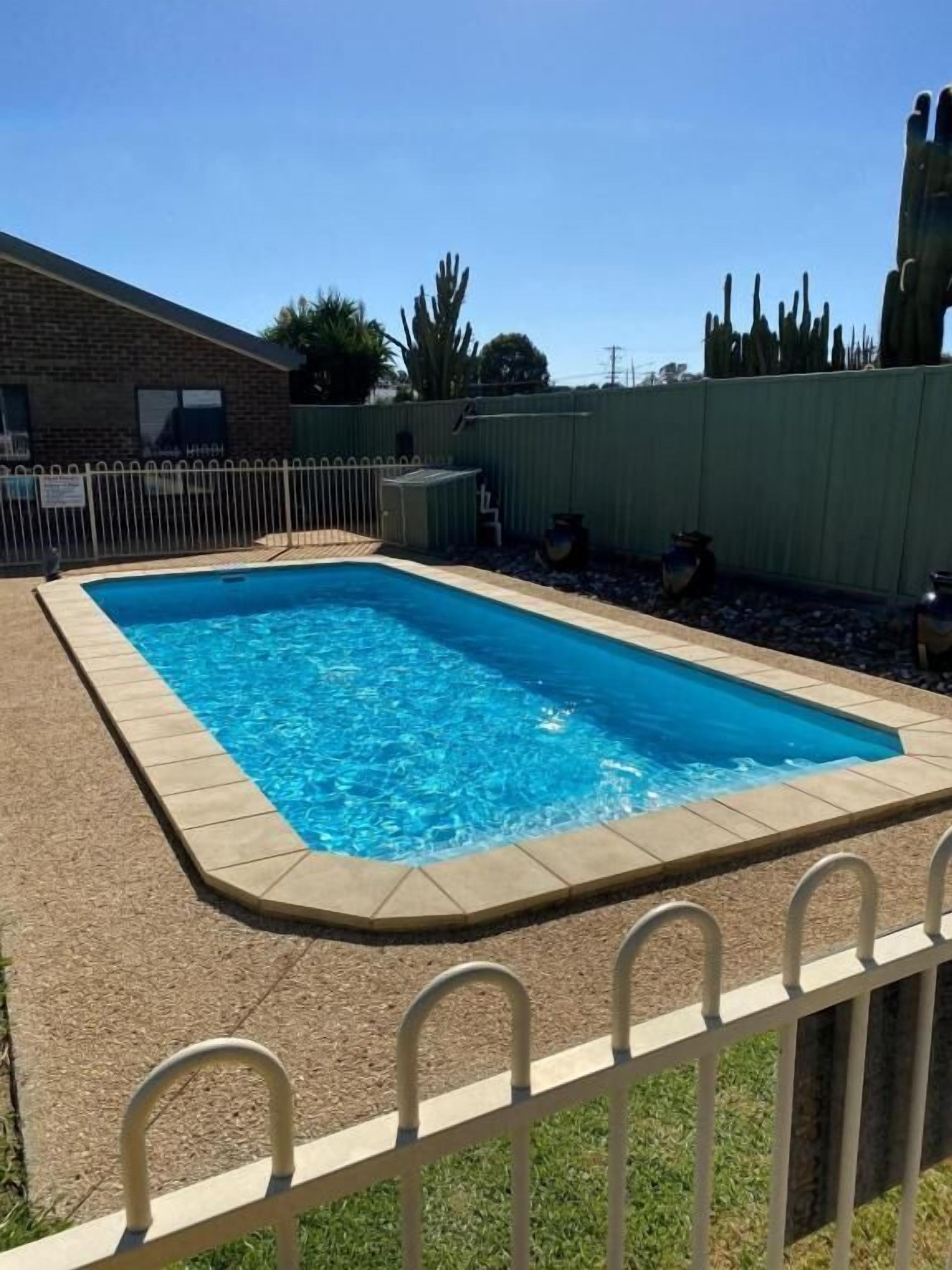 A rectangular swimming pool with a tiled edge, surrounded by a fence and a grassy area.