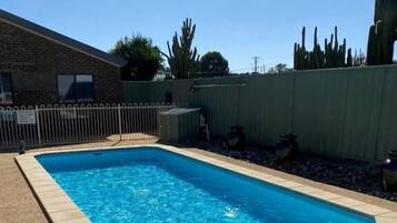 A rectangular swimming pool with a tiled edge, surrounded by a fence and a grassy area.