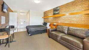 A hotel room with a brick wall, a bed, a sofa, a desk with chairs, and a small table. - Allara Motor Lodge (White Hills)