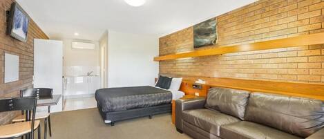 Habitación de hotel con pared de ladrillo, cama, sofá, escritorio con sillas y una mesita.