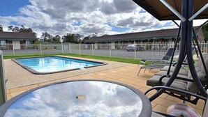 A pool area with a hot tub, lounge chairs, and a view of a residential neighborhood. - Allara Motor Lodge (White Hills)