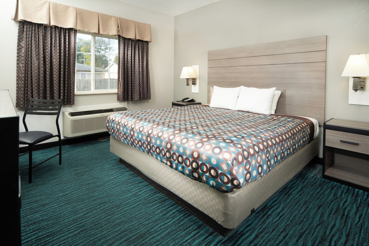 Ein Hotelzimmer mit einem großen Bett, zwei Nachttischen, einem Sessel, einem Schreibtisch und einem Fenster mit Vorhängen.