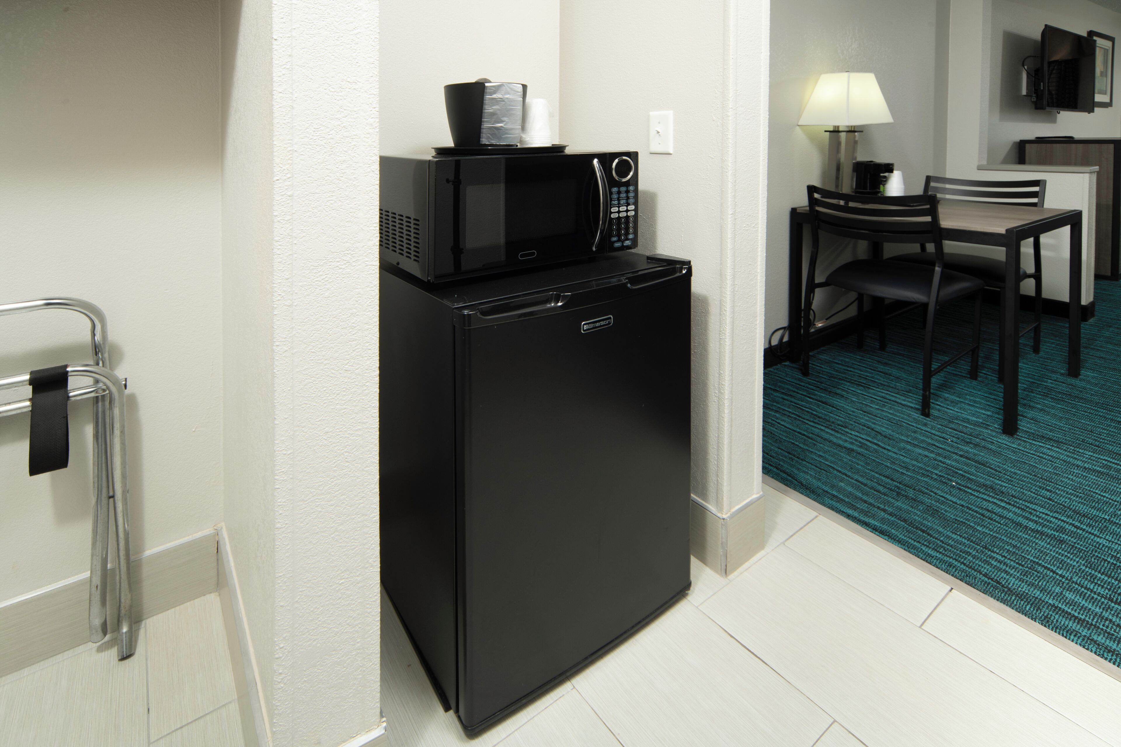 A compact kitchenette with a black refrigerator, microwave, and a small table with a chair.