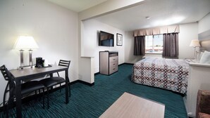 Habitación de hotel con cama, escritorio con silla, una mesita, televisor y ventana con cortinas.