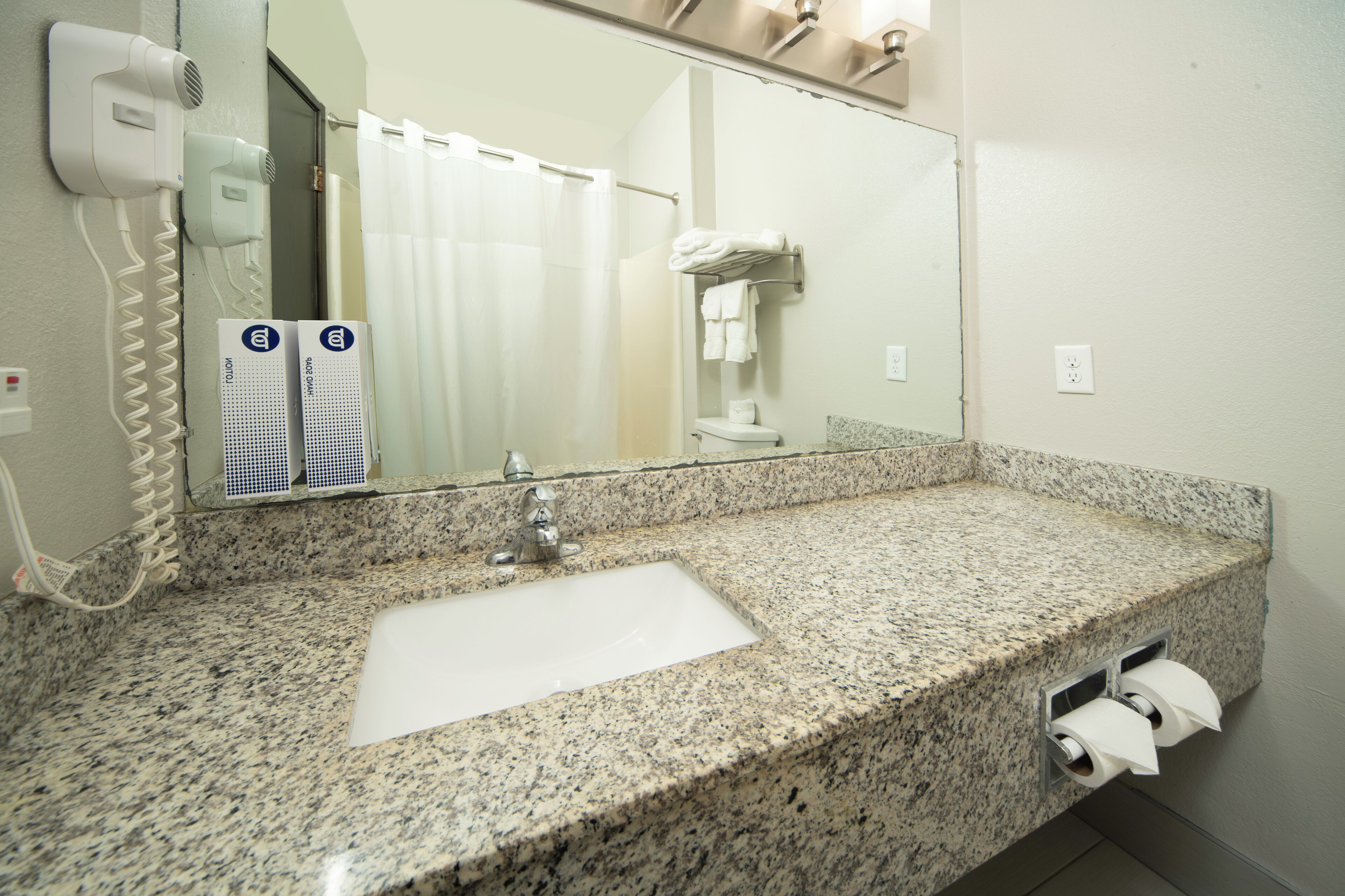 A bathroom with a granite countertop sink, a mirror, a hairdryer, and a towel rack.