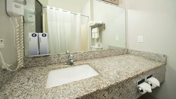 A bathroom with a granite countertop sink, a mirror, a hairdryer, and a towel rack.