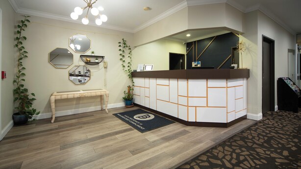 Zona de recepción con suelo de madera, mostrador, banco y espejo en la pared.