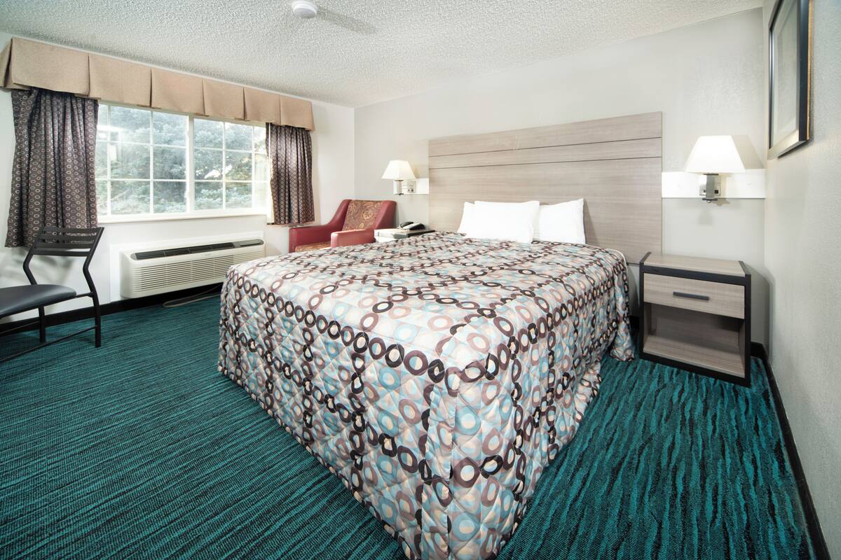 Ein Hotelzimmer mit einem großen Bett, einem Sessel, einem Schreibtisch und einem Fenster mit Vorhängen.