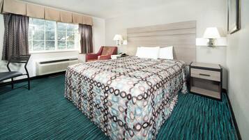 Een hotelkamer met een groot bed, een stoel, een bureau en een raam met gordijnen.