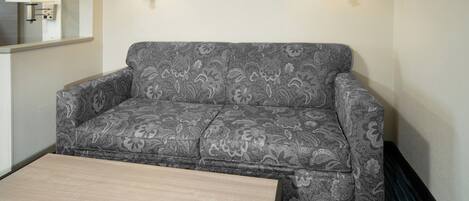 A gray patterned sofa with a wooden coffee table in front, two wall-mounted lamps, and a mirror on the left wall.