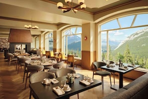 A restaurant with high ceilings, large windows, and a mountain view. - Rimrock Banff, Emblems Collection (Banff)