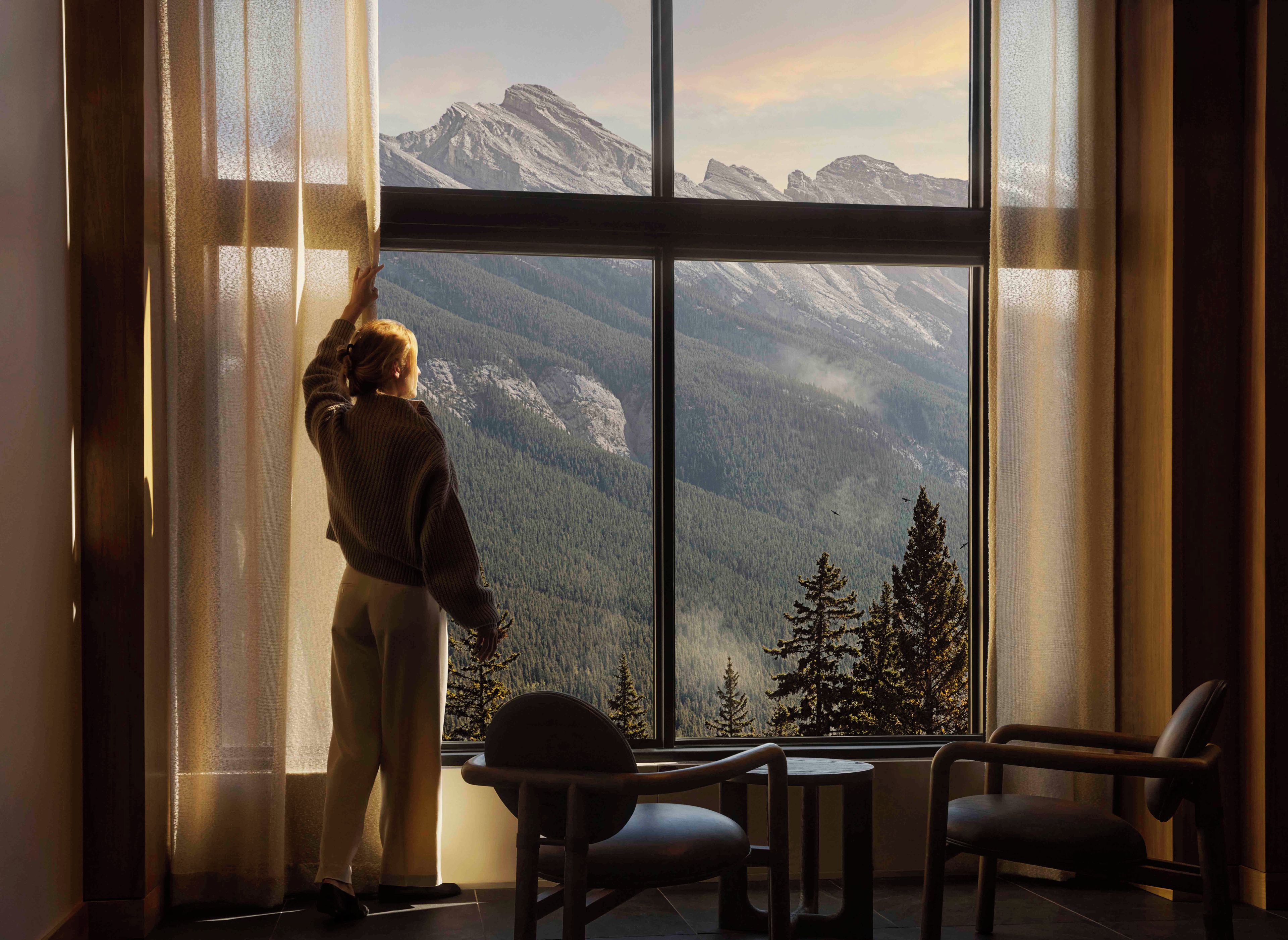 A room with a large window offering a mountain view, a chair, and a small table.